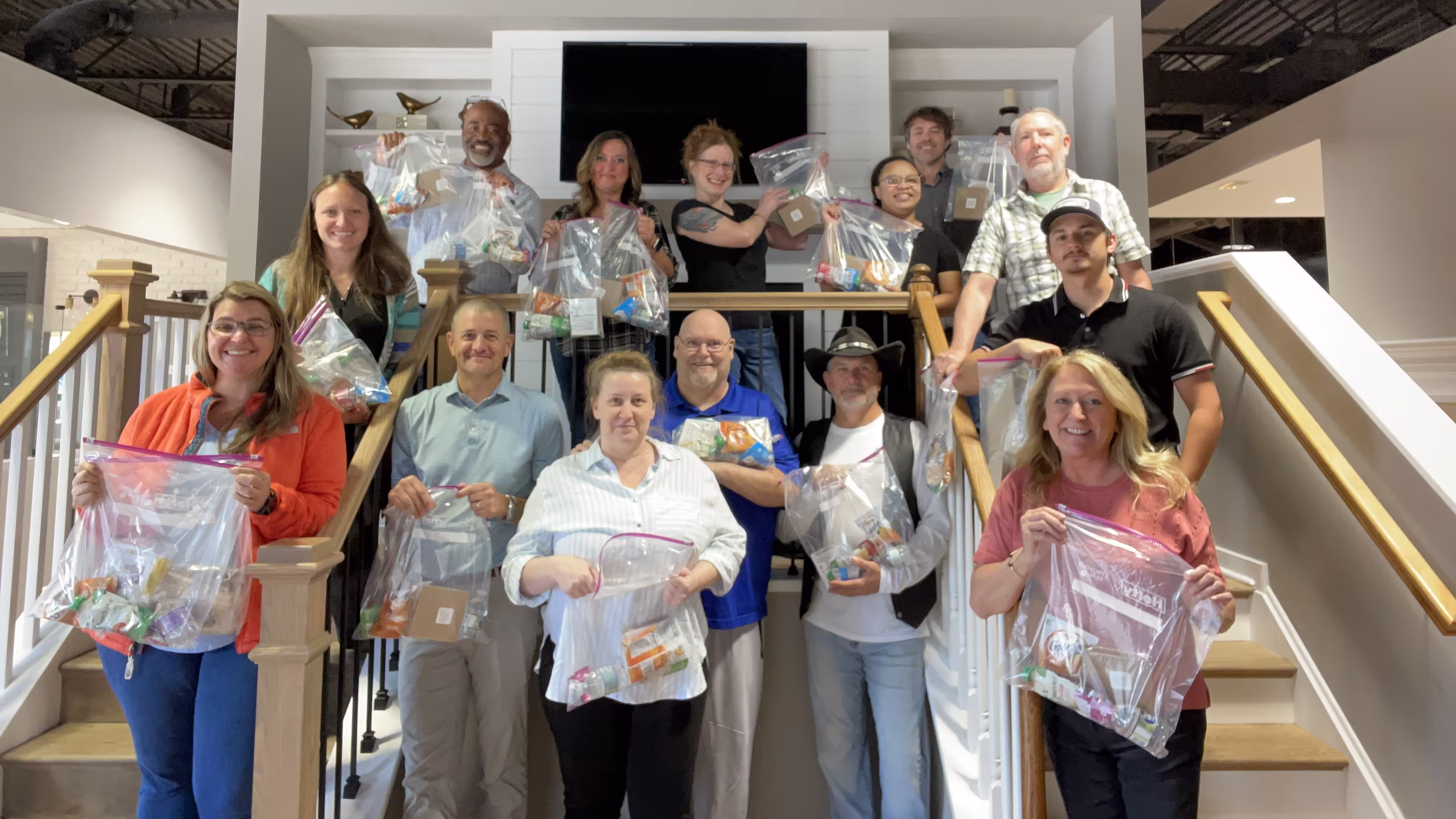 Group of team members standing on a step, holding plastic bags filled with various snack items.