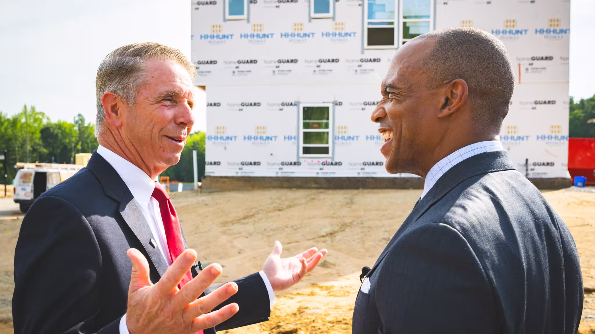 HUD secretary and Congressman facing each other having a conversation with a construction house behind them.