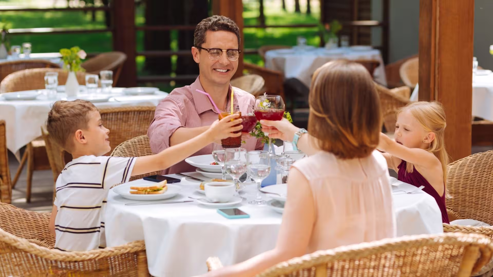 Young family of four at a restaurant doing a "cheers" with glasses.