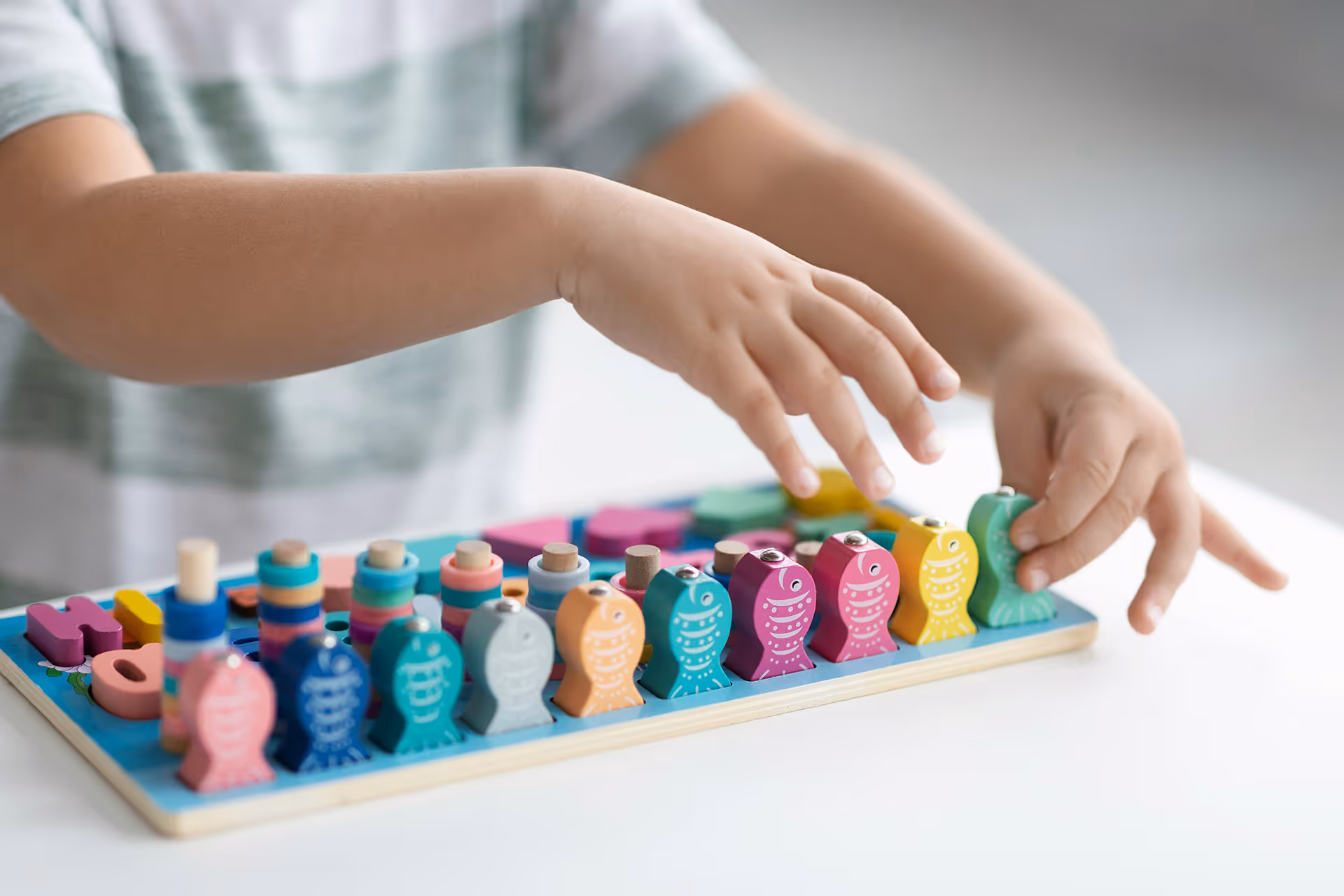 Kind spielt mit buntem Holzspielzeug, das aus Fischen und Stapelringen besteht.