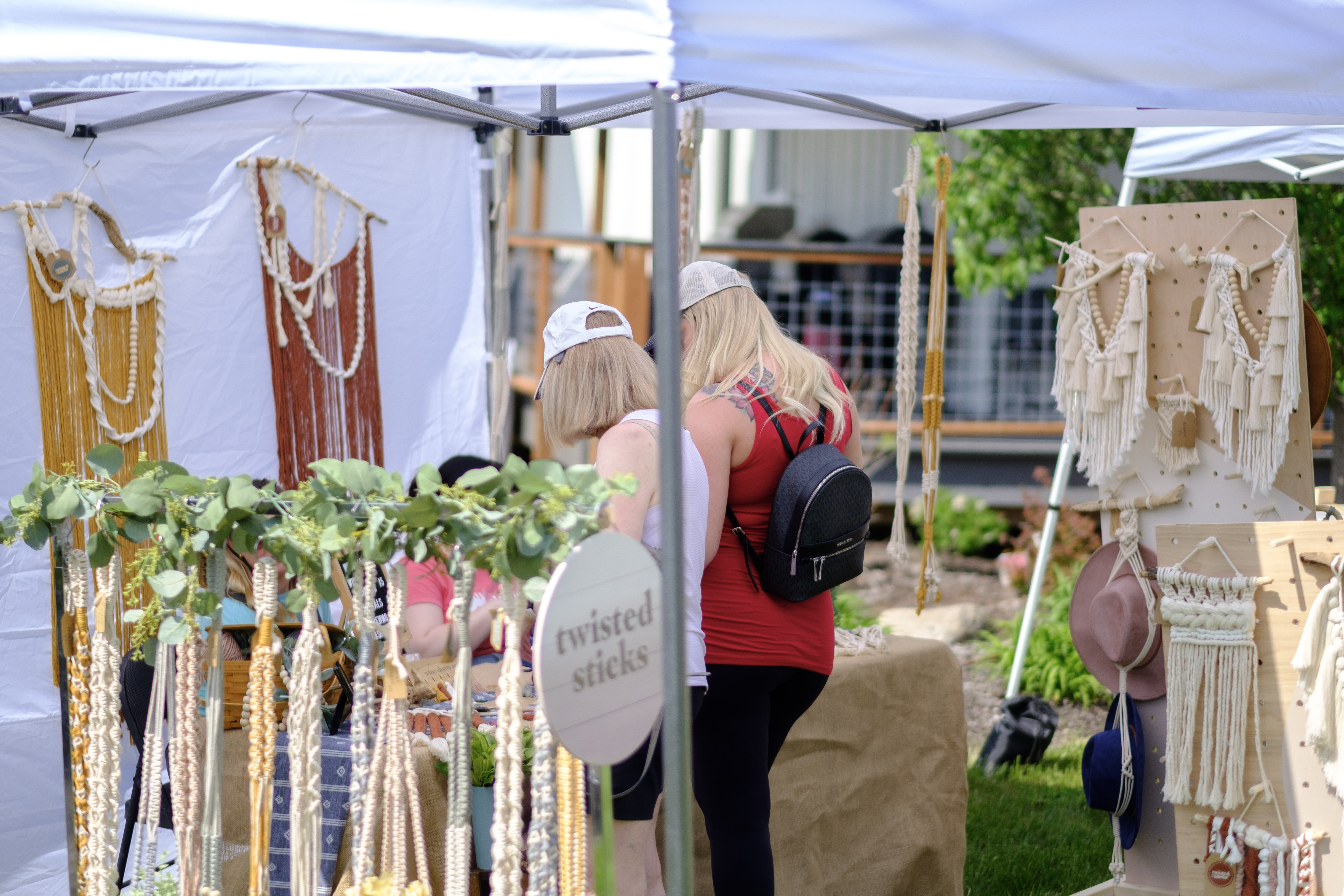 Outdoor marketplace stall with Brown Dog Studio jewelry displayed and vendor sitting behind the table.