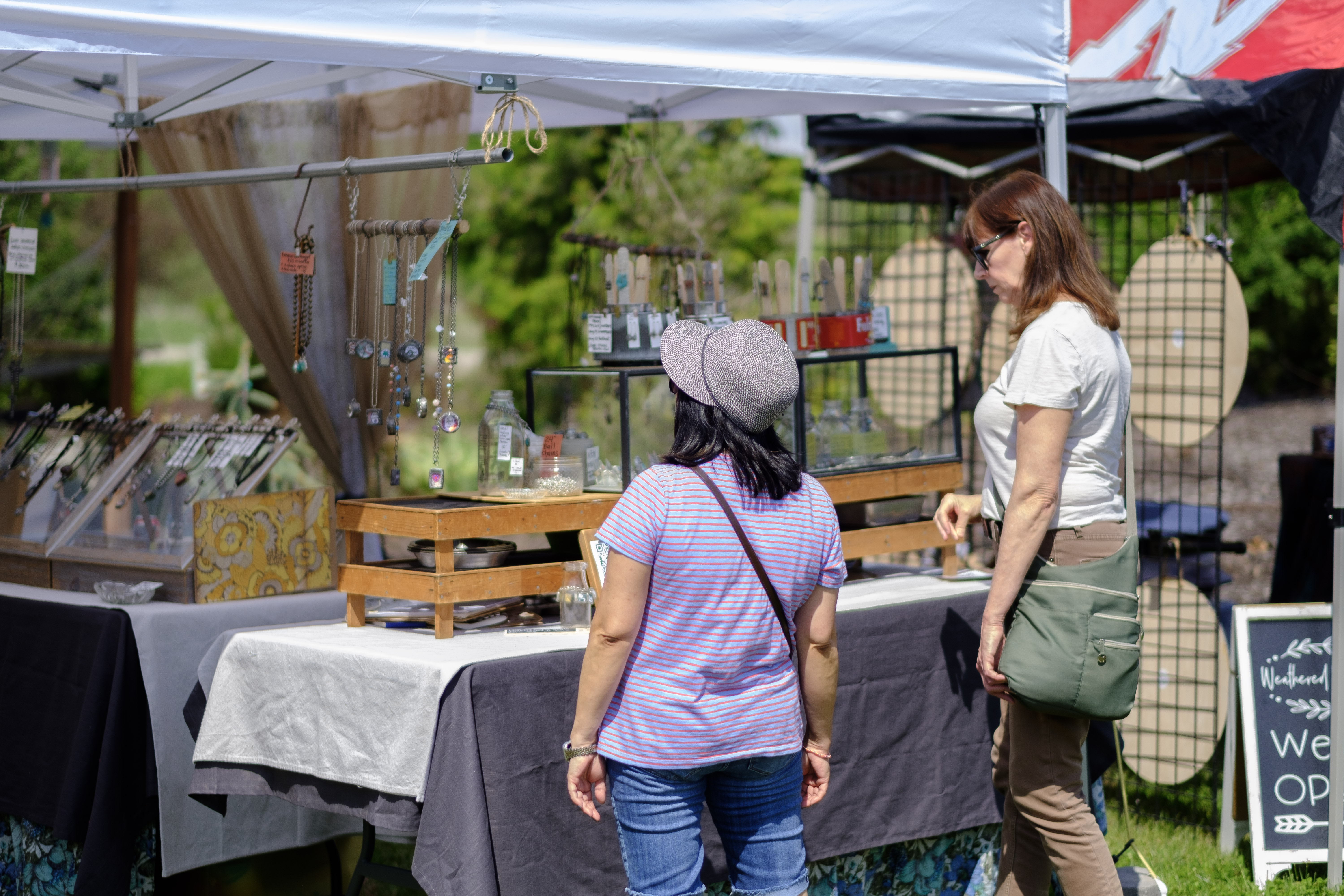 Three people at a Sweet Things baked goods stand with wooden crates and a guitar player in the background.