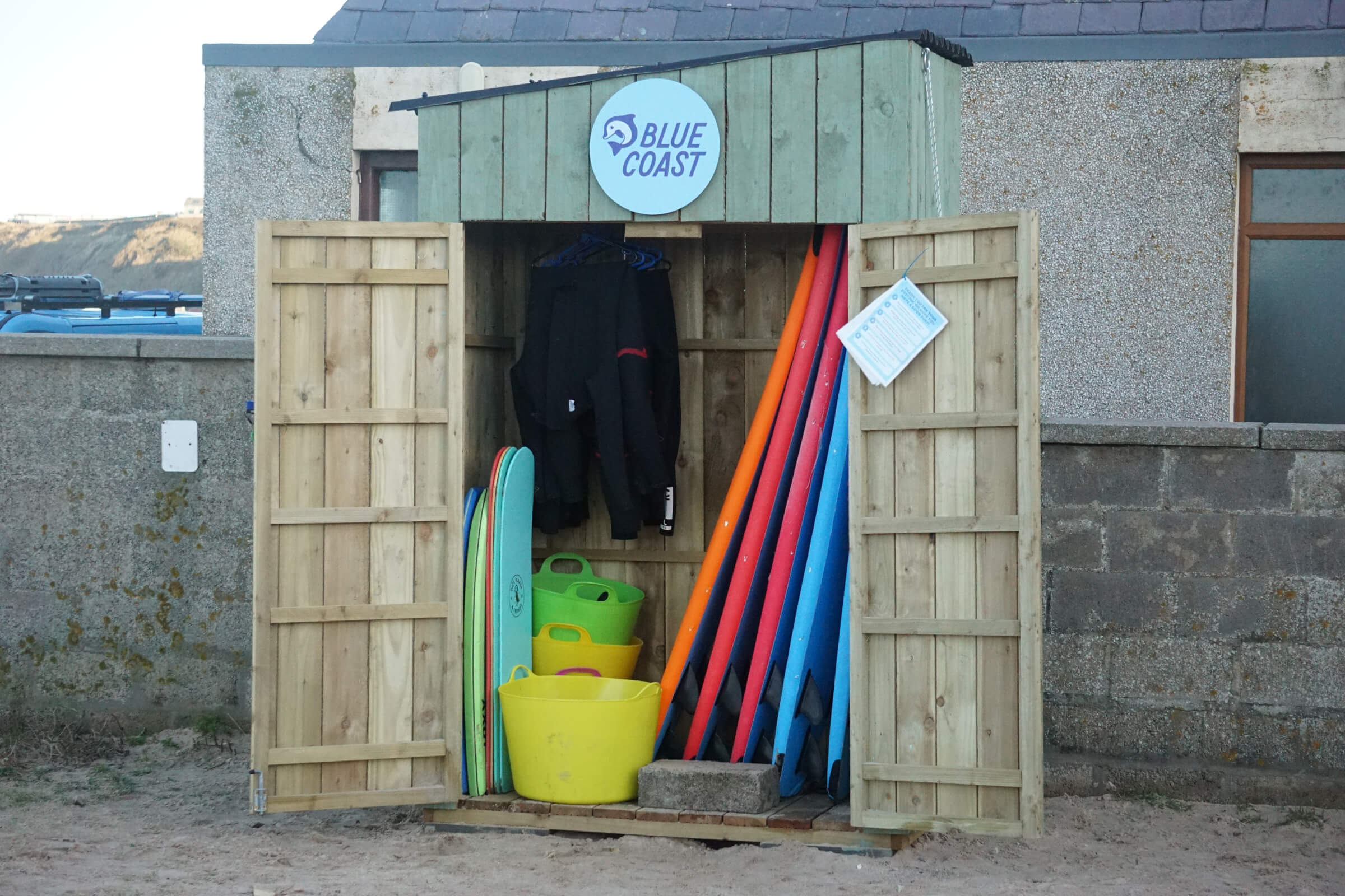 The Blue Coast Self-Service Surf Hire Kiosk at Cullen Beach with its doors open and a range of surfboards and wetsuits visible inside.