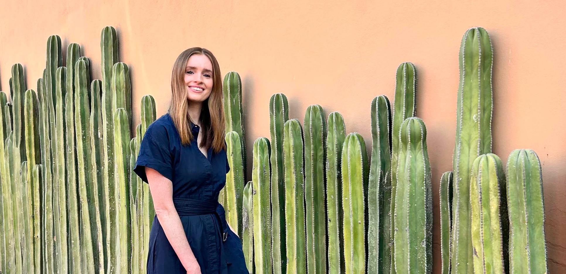 Image of Juliette in Mexico, wearing a navy dress and standing in front of a row of cacti