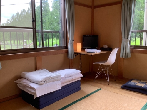 Hifumikan's room corner with a futon, chair & desk with tree views