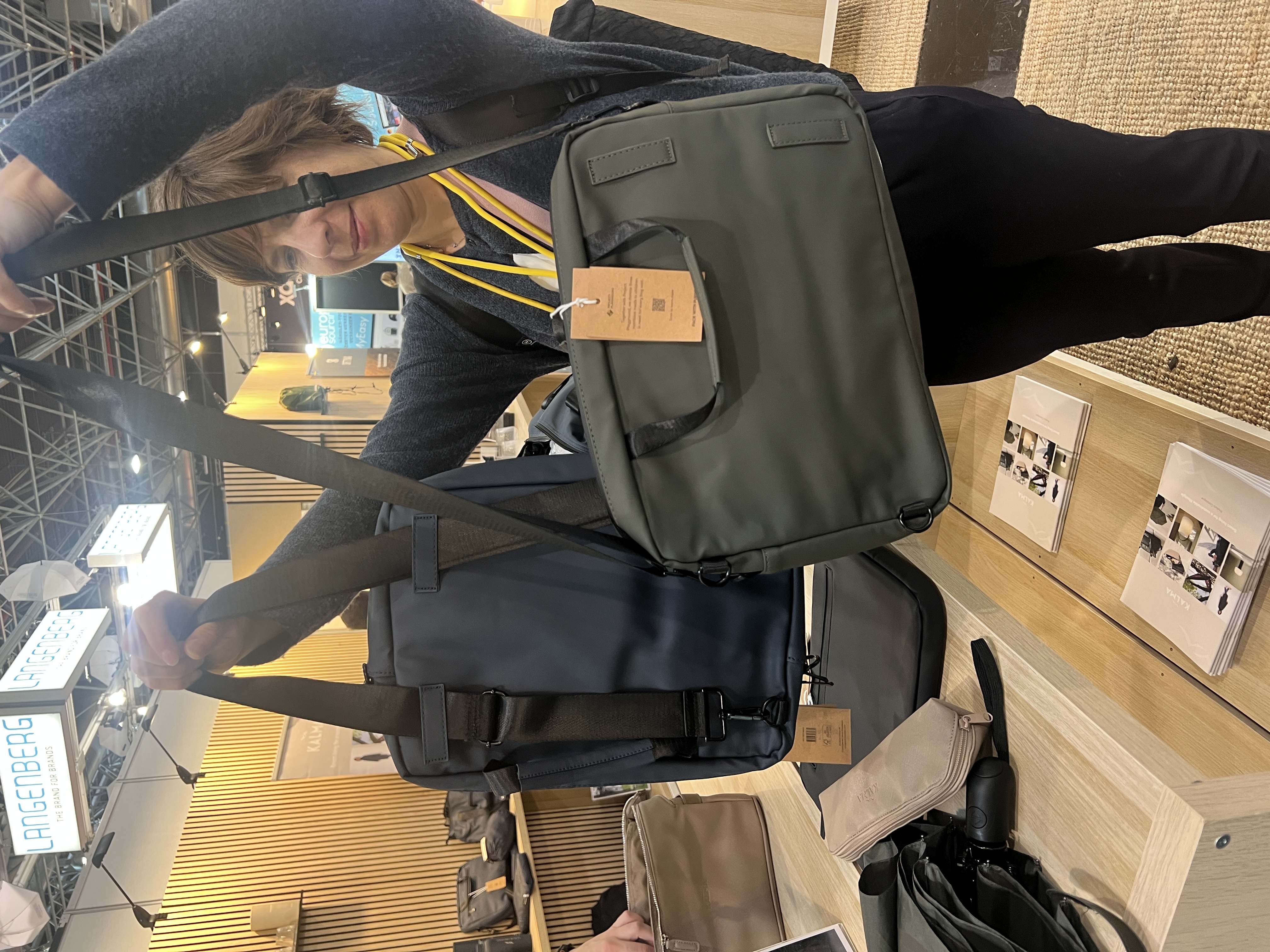 Frau vergleicht einen blauen Rucksack und eine olivgrüne Laptoptasche als Werbeartikel-Auswahl 2026‍