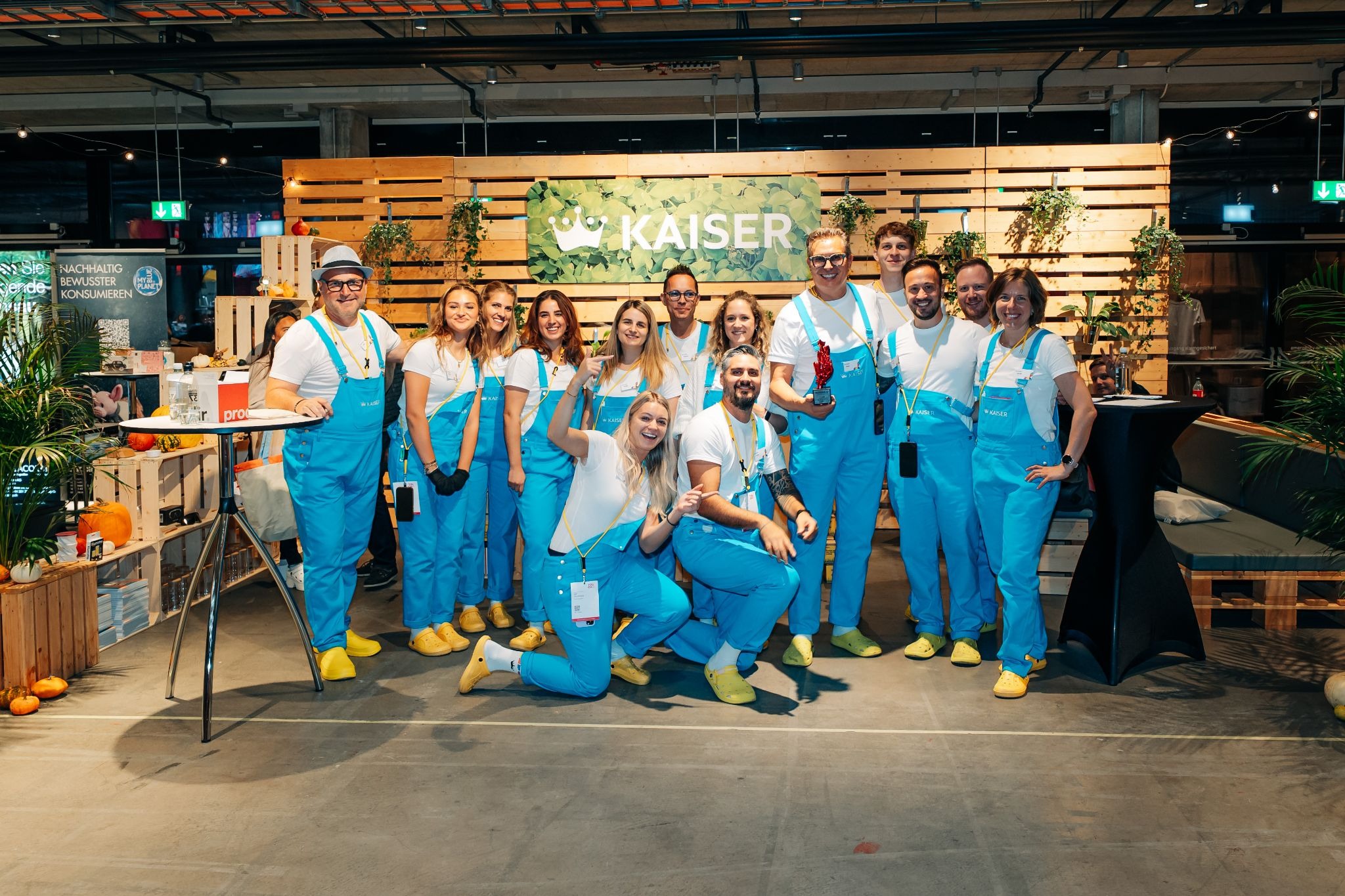 Das Kaiser-Team mit blauen Latzhosen und gelben Crocs Schuhen vor dem Messestand zum Thema Wachstum.