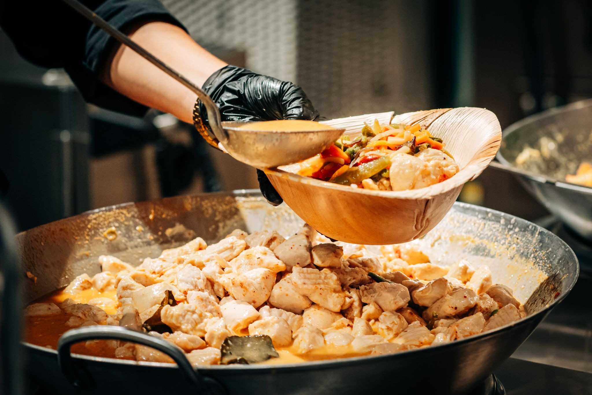 Catering-Mitarbeiter schöpft Thai-Curry mit Poulet und Reis