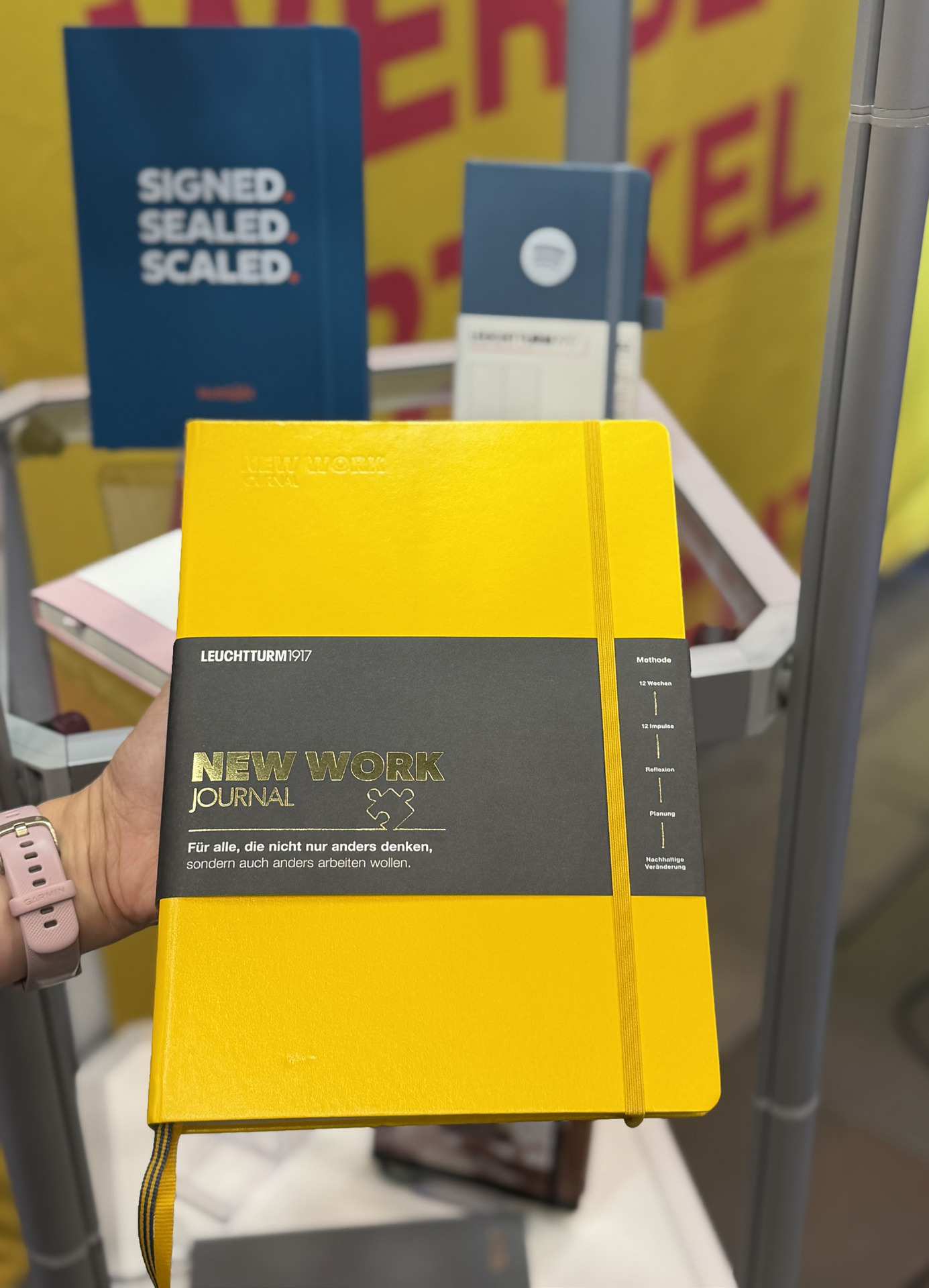 Gelbes New Work Journal von Leuchtturm1917 mit schwarzem Banderolen-Label, in der Hand gehalten am Messestand