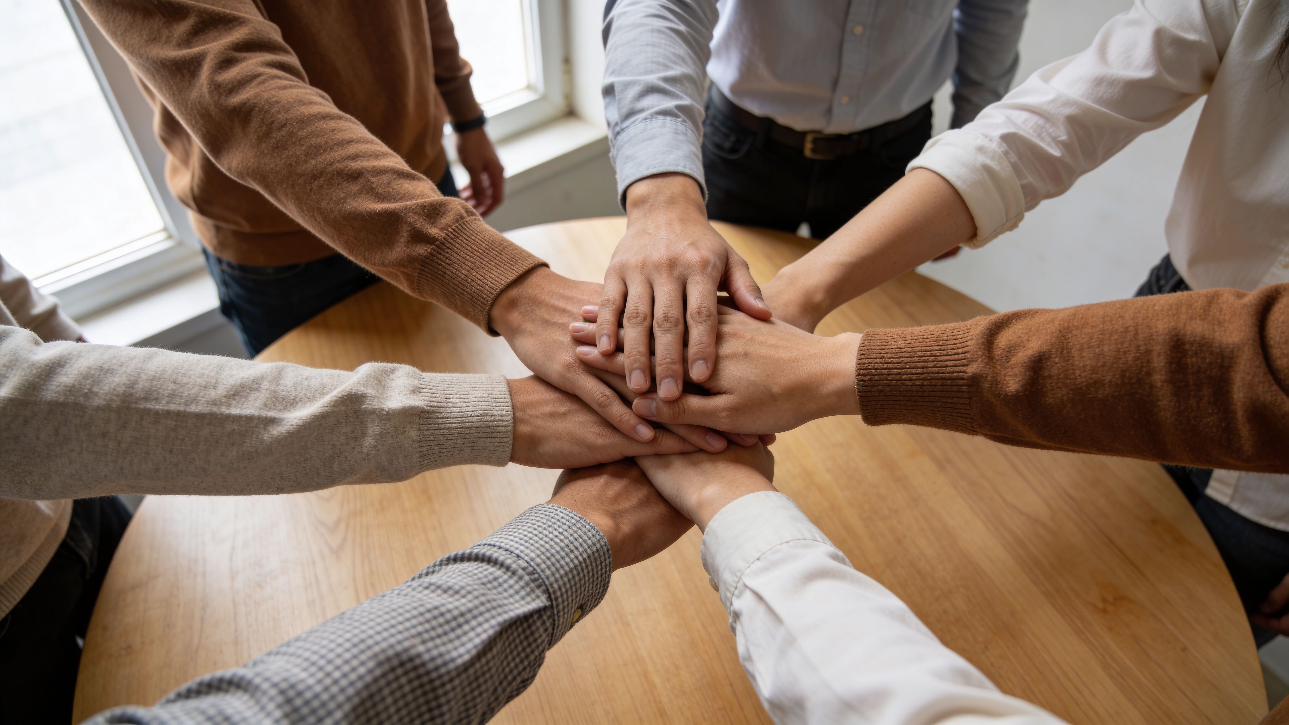 Un grupo de personas uniendo sus manos en el centro como símbolo de trabajo en equipo.