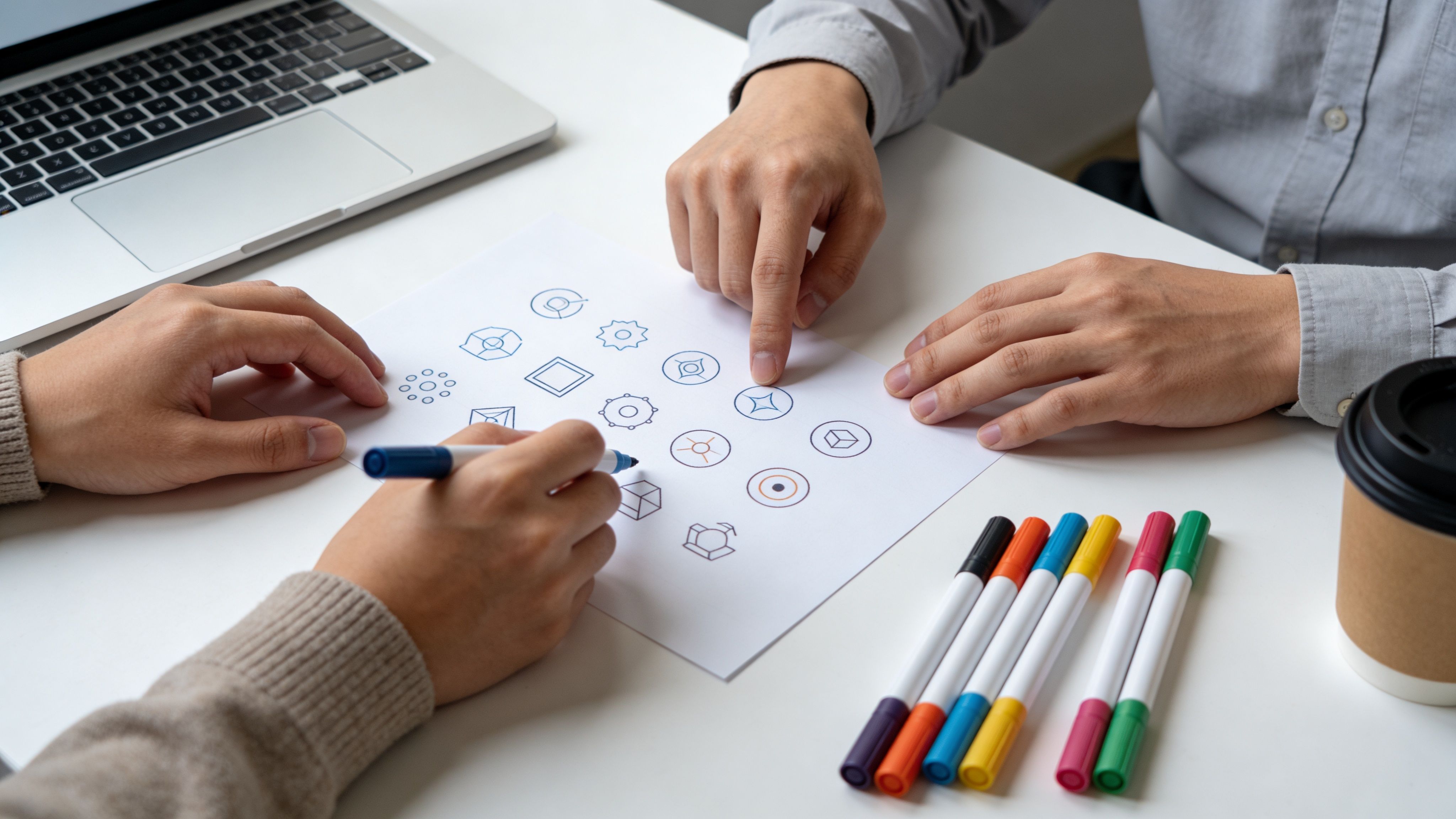 Dos personas trabajando juntas en el diseño de logotipos sobre papel blanco en una oficina moderna.