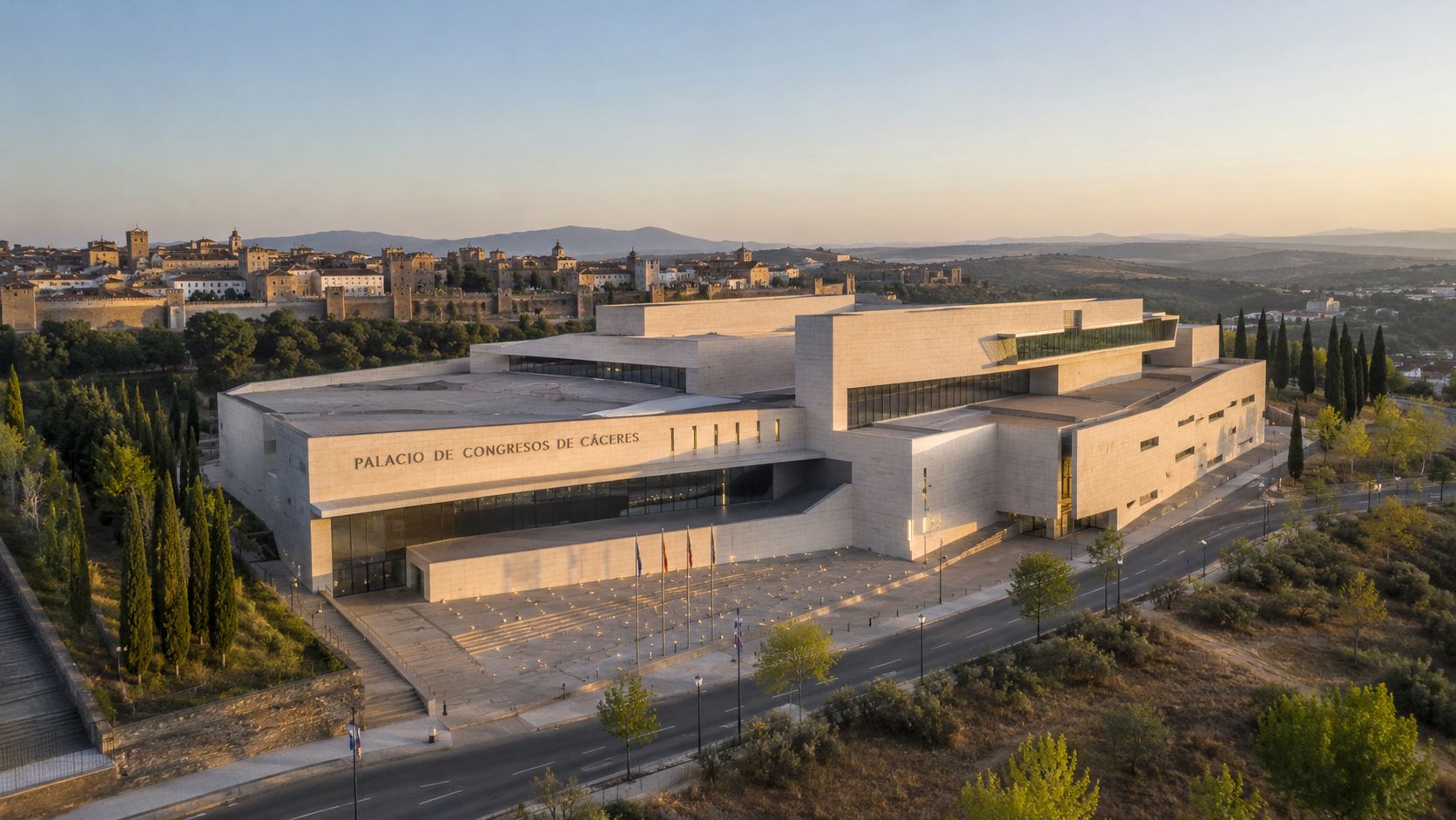 Vista aérea al atardecer del Palacio de Congresos de Cáceres, España, rodeado de naturaleza y arquitectura histórica.