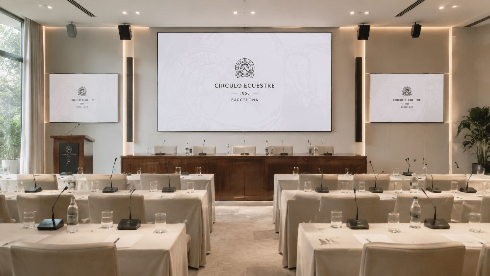 Sala de conferencias elegante con pantallas que muestran el logotipo del Circulo Ecuestre de Barcelona.