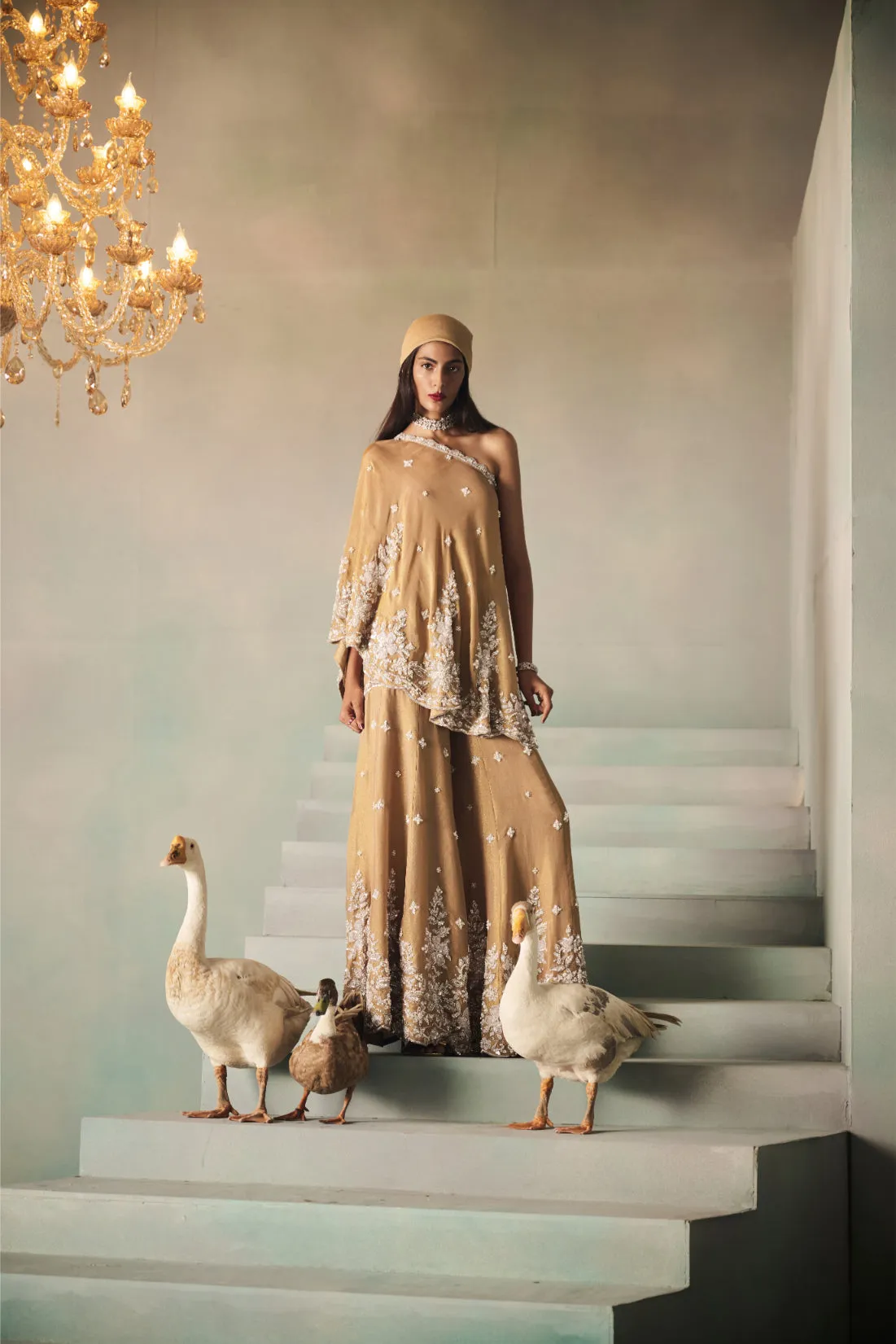 A contemporary classic, this golden kaftan set exudes refined elegance with its asymmetric one-shoulder silhouette. Adorned with delicate white embroidery and sequins cascading along the hemline, the flowing top is paired with wide-leg trousers for a regal yet effortless look. A perfect blend of modern chic and timeless tradition, ideal for festive evenings and soirées.
