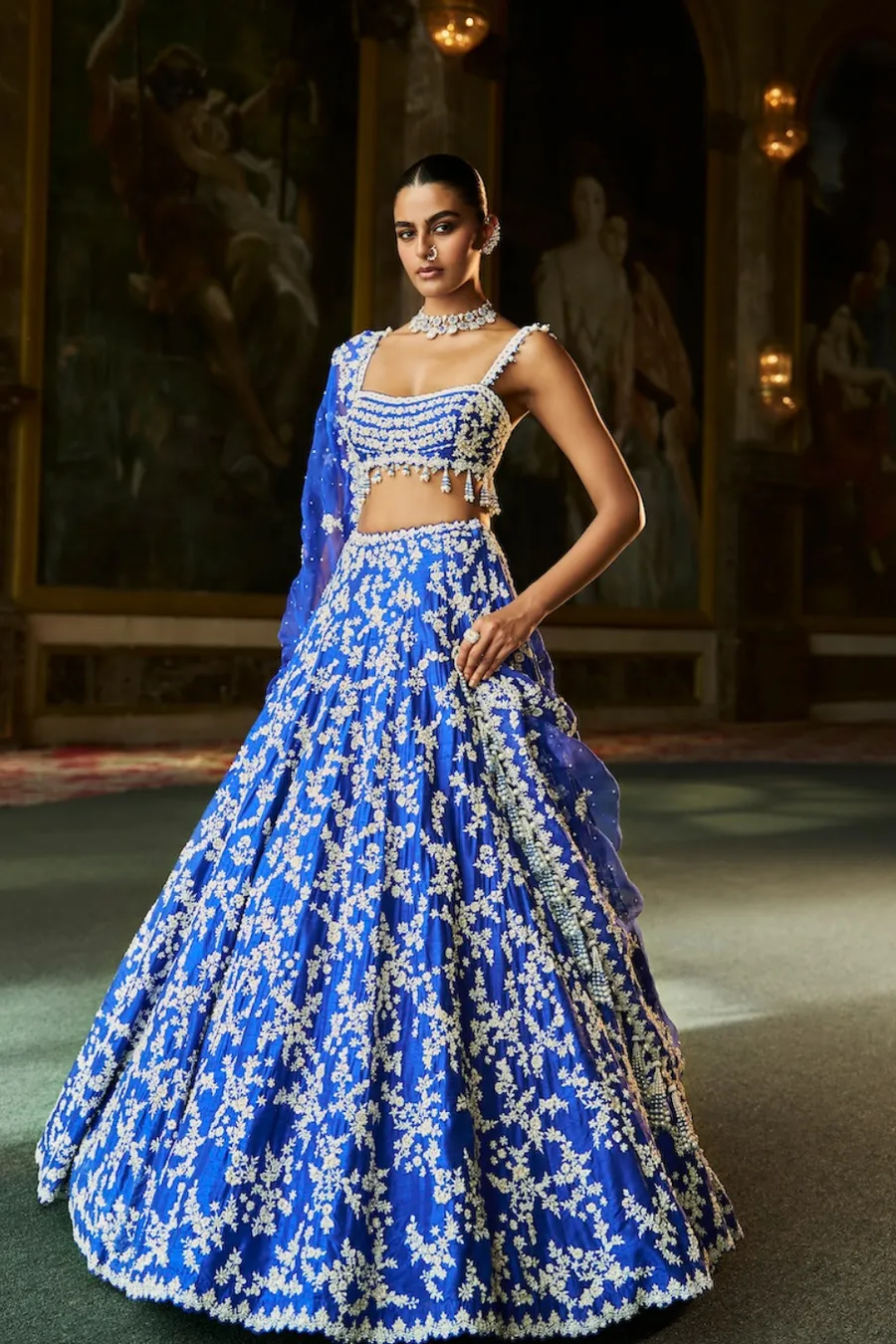 This emerald green lehenga is a luminous ode to nature-inspired couture, adorned with intricate ivory floral embroidery that cascades gracefully across the silhouette. The exquisitely crafted blouse features ornate handwork and delicate edging, creating a harmonious balance of structure and softness. A matching dupatta, lightly embellished, frames the ensemble with refined elegance and fluid movement. Fresh yet opulent, this creation embodies timeless artistry with a celebratory, regal presence.