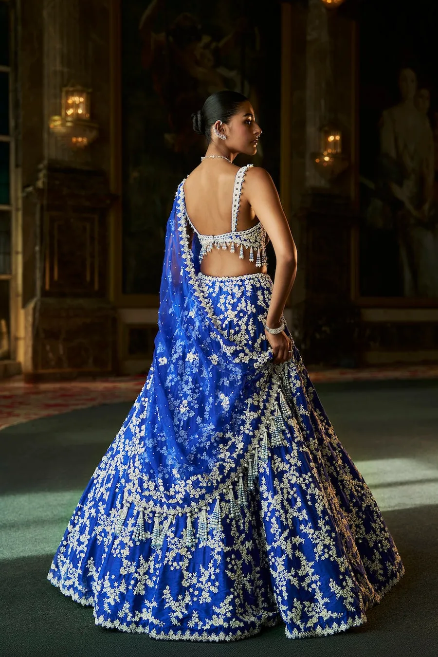 This emerald green lehenga is a luminous ode to nature-inspired couture, adorned with intricate ivory floral embroidery that cascades gracefully across the silhouette. The exquisitely crafted blouse features ornate handwork and delicate edging, creating a harmonious balance of structure and softness. A matching dupatta, lightly embellished, frames the ensemble with refined elegance and fluid movement. Fresh yet opulent, this creation embodies timeless artistry with a celebratory, regal presence.