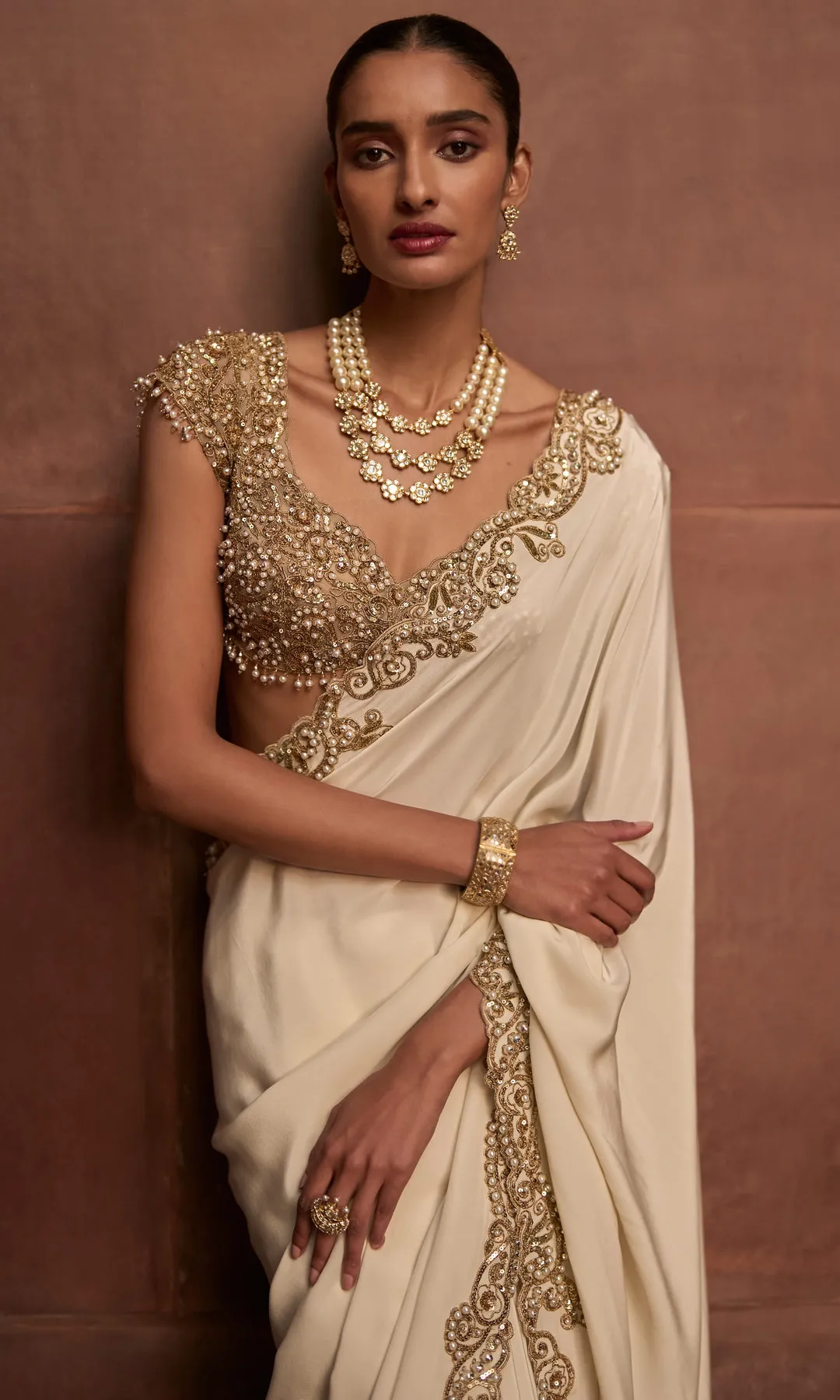 Zameen-e-Noor is a regal bridal sharara ensemble crafted in a rich antique gold tone, celebrating traditional craftsmanship with timeless elegance. The voluminous sharara pants are adorned with intricate all-over hand embroidery featuring geometric and floral motifs, highlighted with zardozi, sequins, and fine beadwork. Paired with a heavily embellished short kurta and finished with a delicately embroidered sheer dupatta, this ensemble exudes ceremonial grandeur. Designed for brides seeking heritage luxury with a distinguished silhouette, it is an ode to classic bridal opulence.