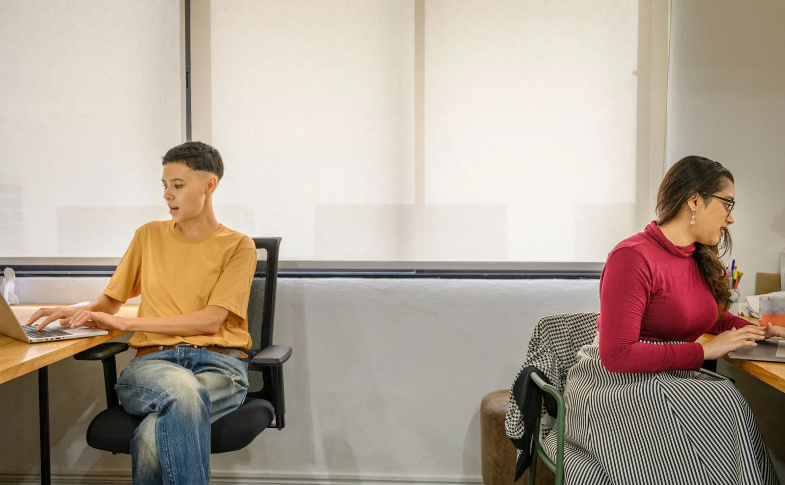 Zwei Mitarbeitende arbeiten an Laptops an getrennten Schreibtischen in einem hellen Büro