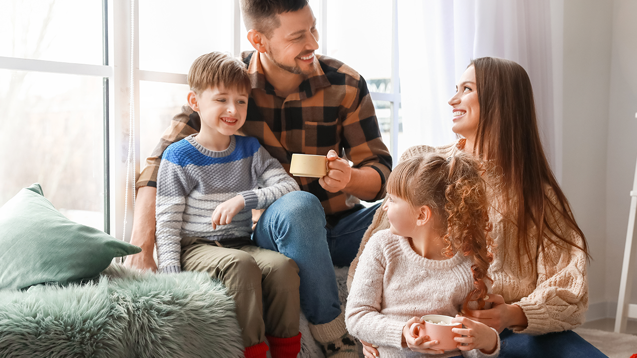 Happy family sitting by a window enjoying hot drinks together