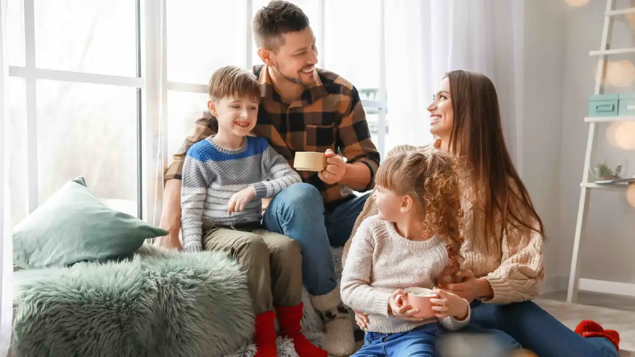 Happy family sitting by a window enjoying hot drinks together