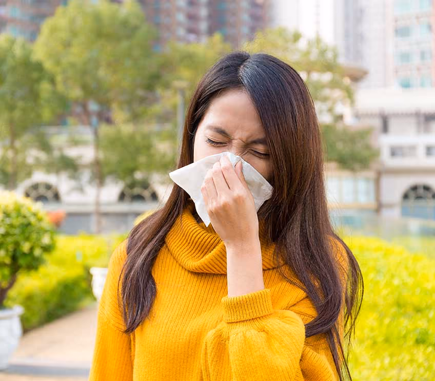 Young woman blowing her nose outdoors showing allergy discomfort