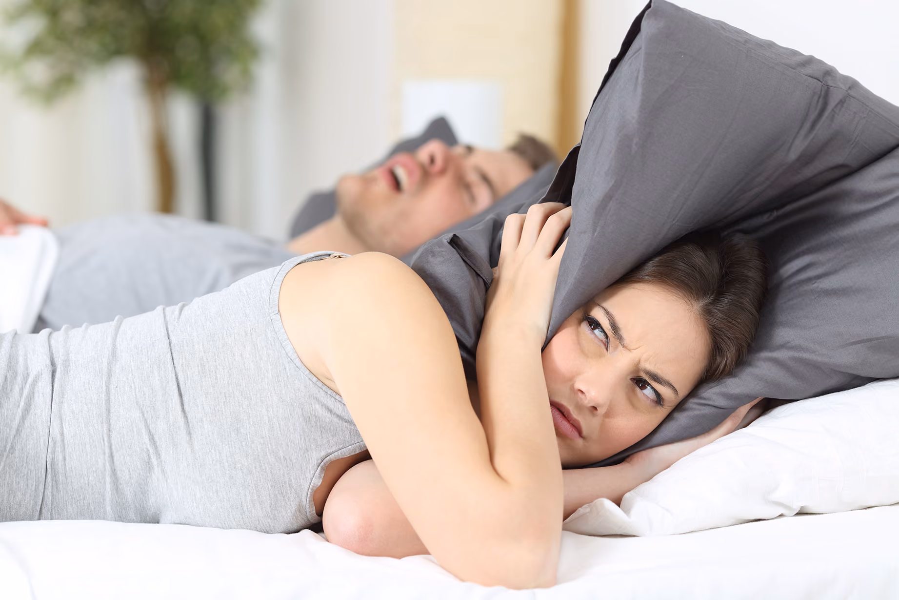 Frustrated woman covering her ears while partner snores beside her in bed