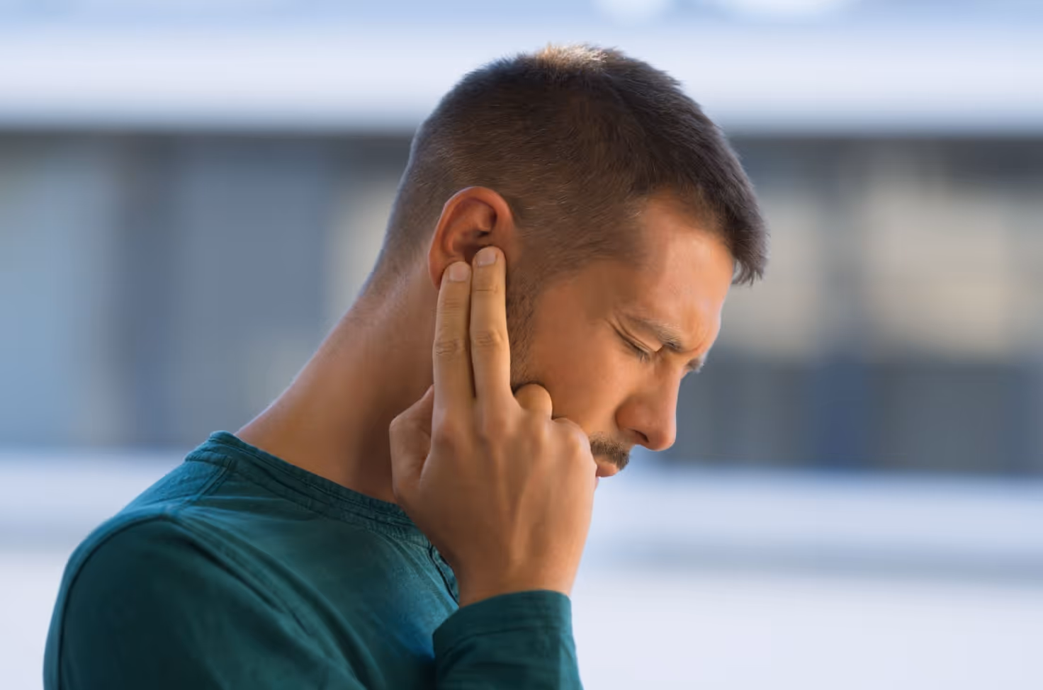 Man pressing his ear in discomfort, representing symptoms of ear pressure and Eustachian Tube Dysfunction.