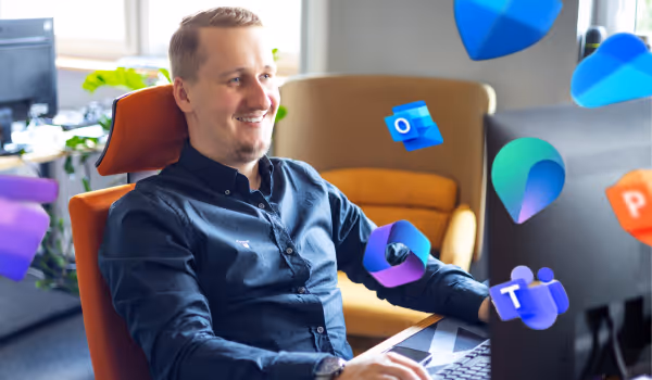 Mężczyzna uśmiecha się siedząc przy komputerze z unoszącymi się ikonami aplikacji Microsoft Office.