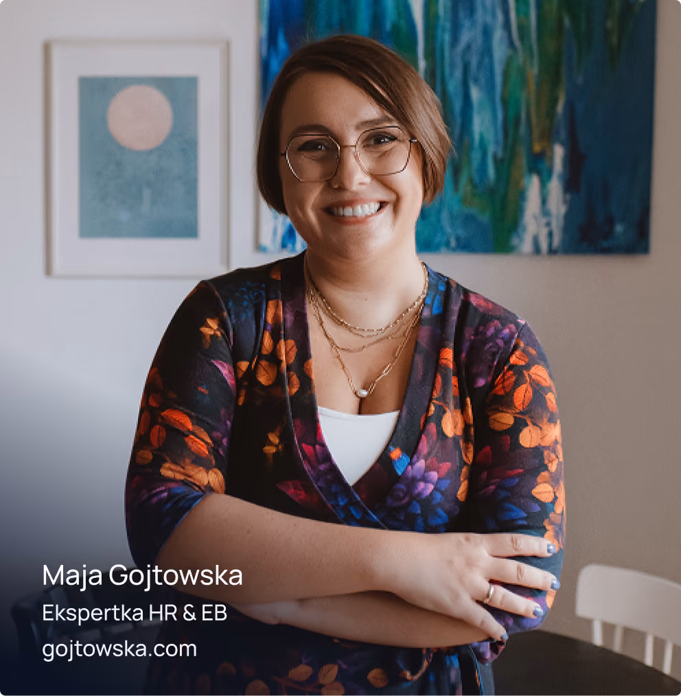 Portret uśmiechniętej Mai Gojtowskiej w okularach i kwiecistej sukience, ze skrzyżowanymi ramionami, na tle pomieszczenie z obrazami. Na zdjęciu widoczny napis: Maja Gojtowska, Ekspertka HR & EB, gojtowska.com.