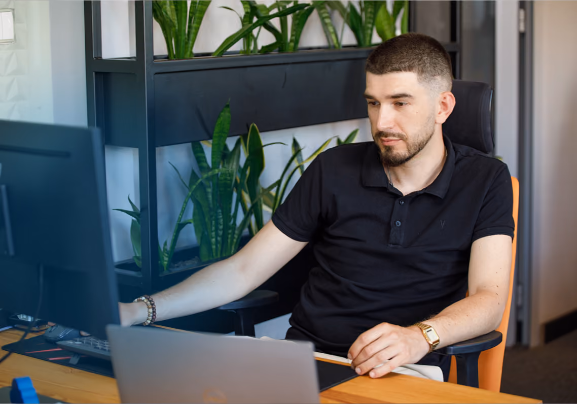 Mężczyzna siedzi przy biurku, patrząc na monitor komputera, w nowoczesnym biurze z roślinami.
