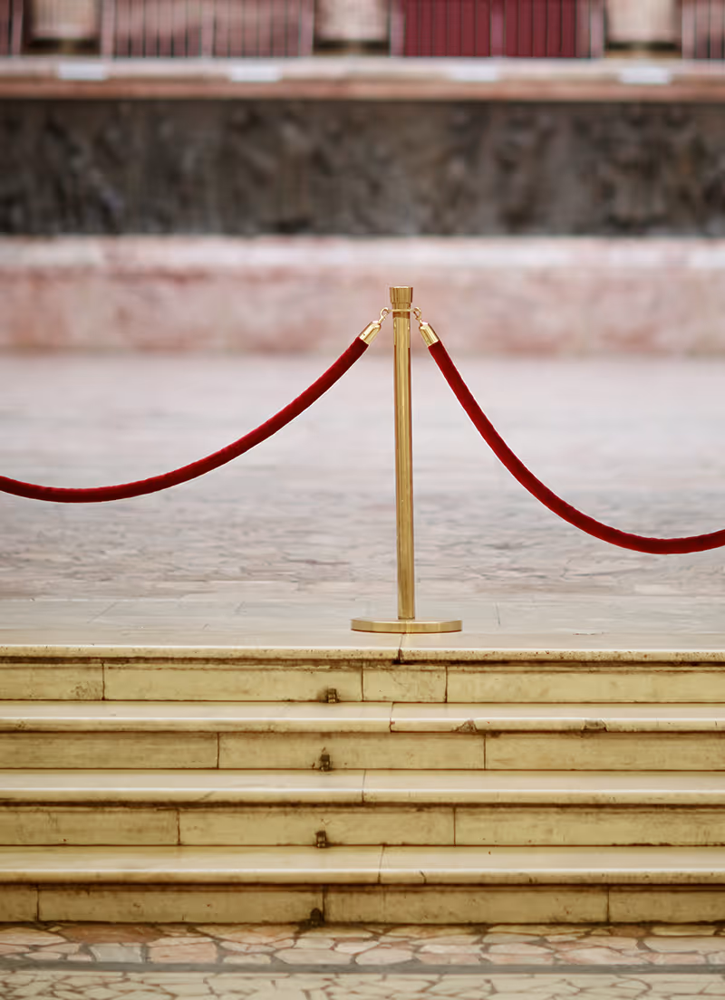 Staircase topped with red velveted rope attached to golden posts.   