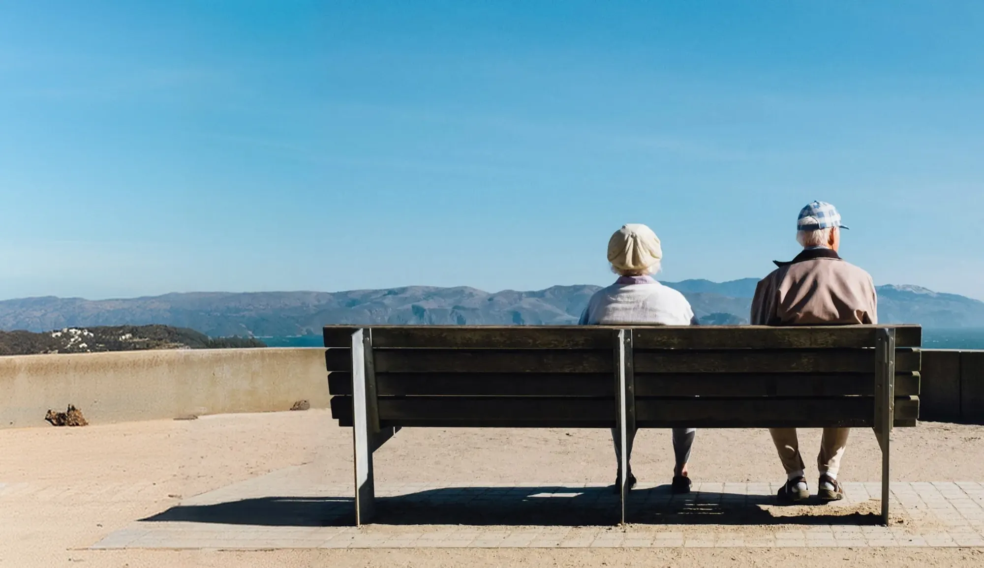 An older couple sitting on a bench looking out over the water