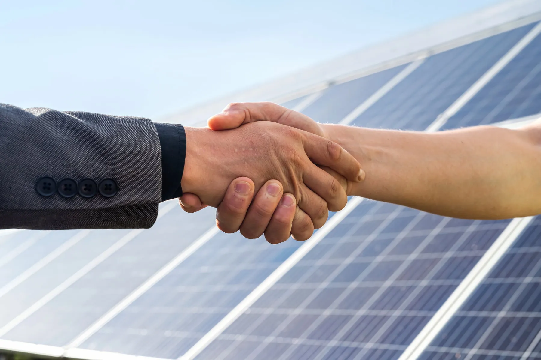 photo of shaking hands in front of solar panels