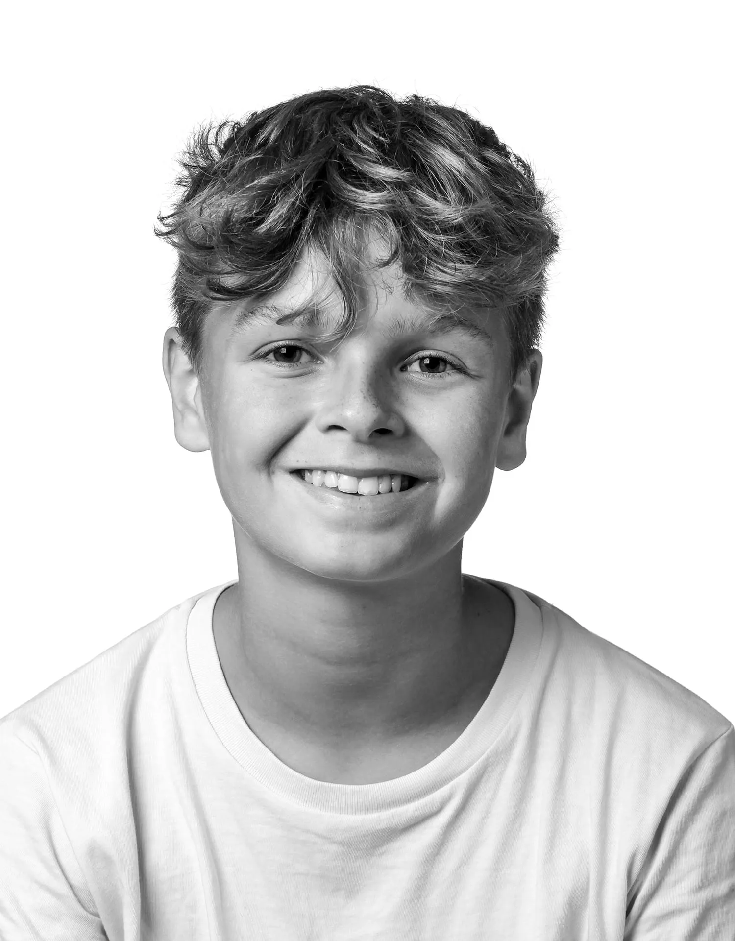 Skolefografi - Smilende dreng med bølget hår i hvid T-shirt foran hvid baggrund – klassisk skolefoto af elev.