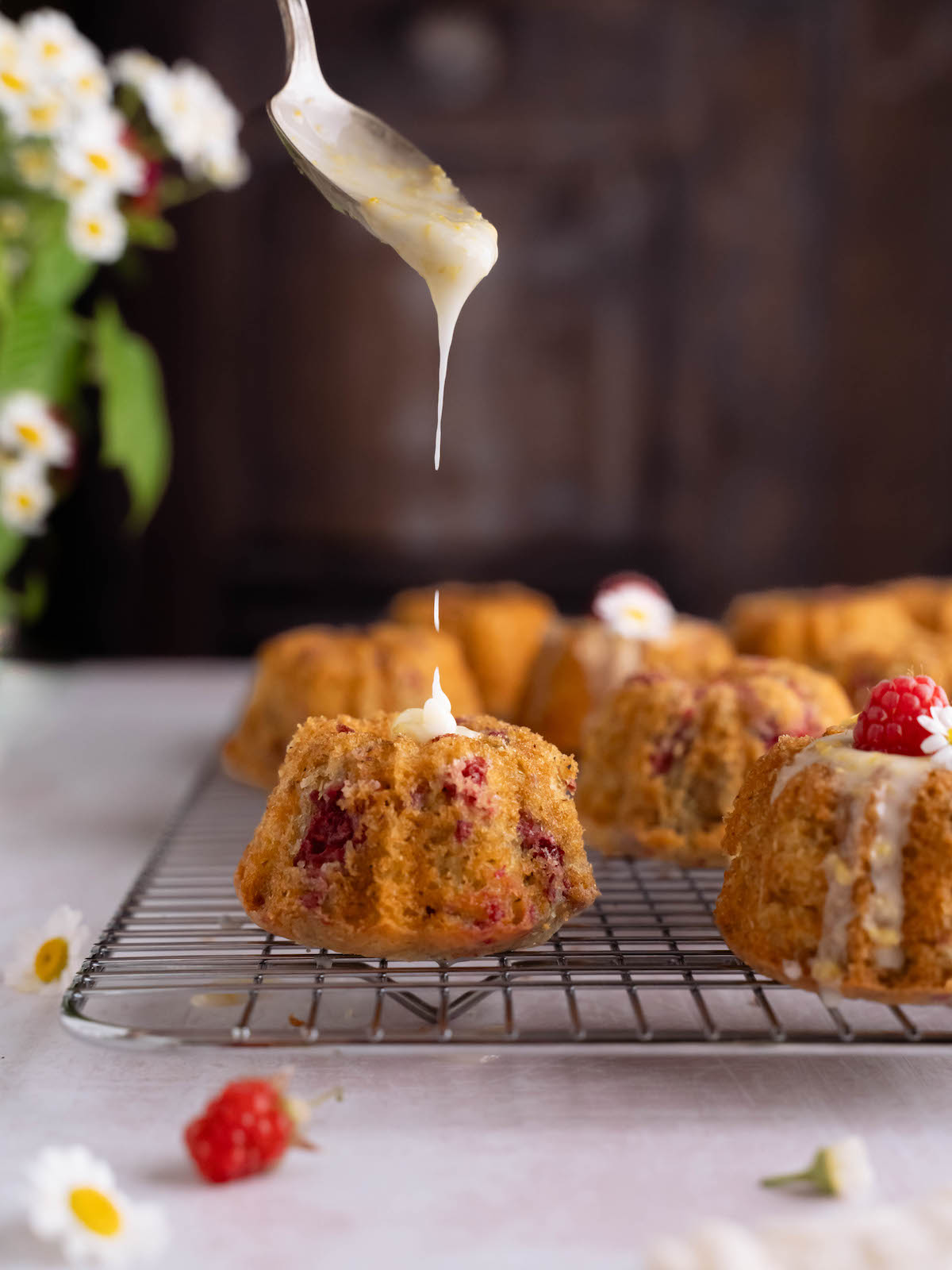 Drizzling lemon glaze onto mini raspberry cakes