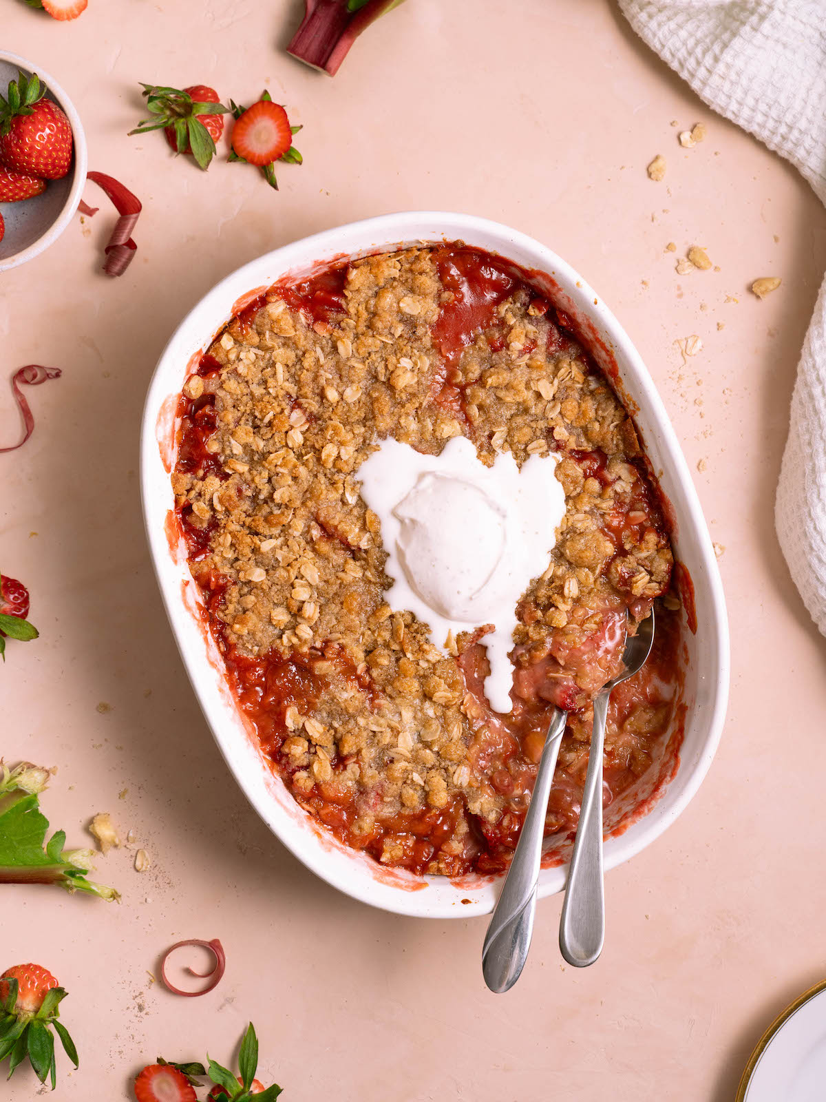 A strawberry rhubarb crisp with whipped cream melting on top