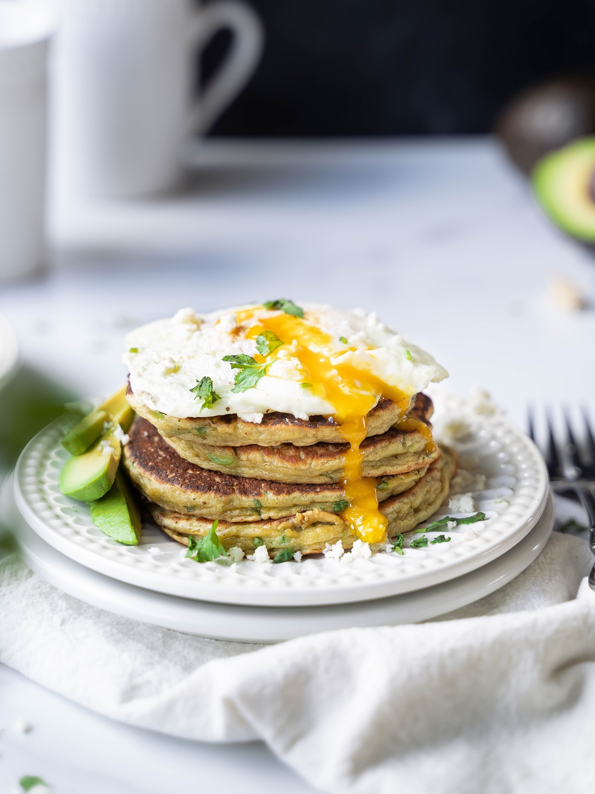 A stack of avocado pancakes with an egg on top