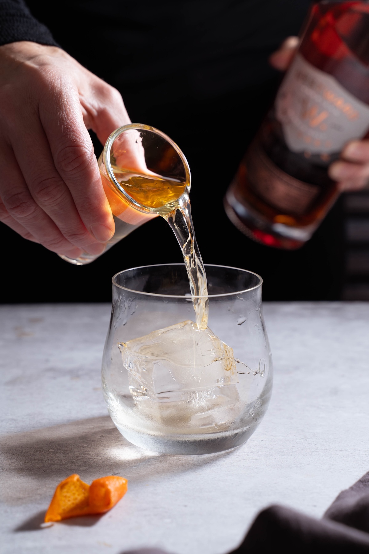 Pouring whiskey into a lowball glass over a big cube