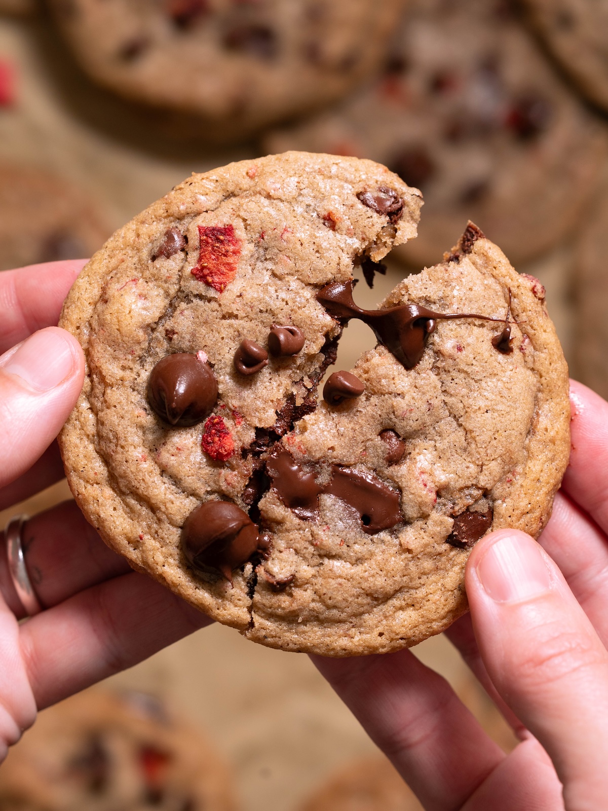 Hands breaking open a gooey strawberry chocolate chip cookie