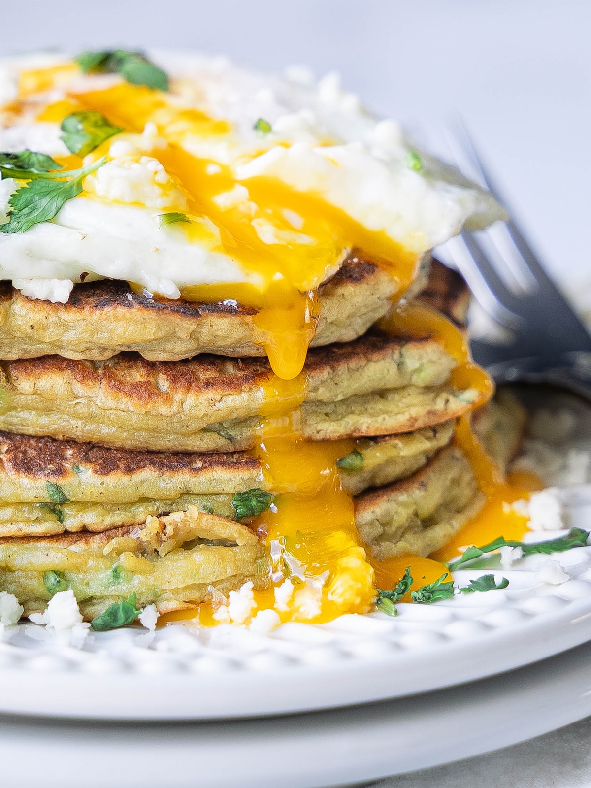 Closeup on a stack of avocado pancakes with egg yolk dripping down the sides