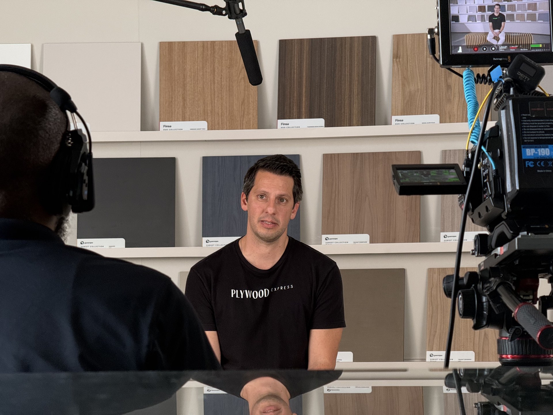 Plywood Express BTS — over-shoulder interview, PLYWOOD EXPRESS shirt clearly visible, camera monitor right