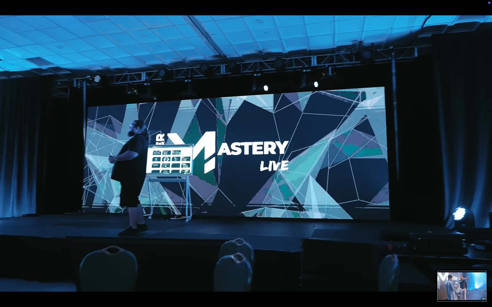 Presenter on stage in front of a large geometric LED backdrop