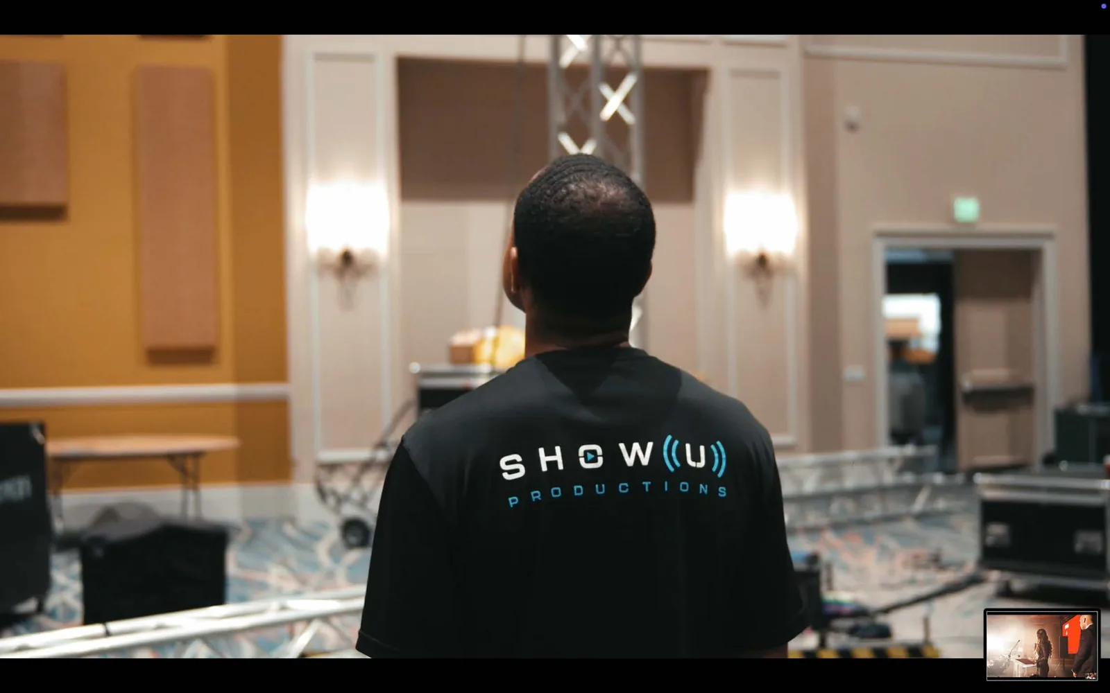 Production technician in a branded crew shirt facing the stage backstage