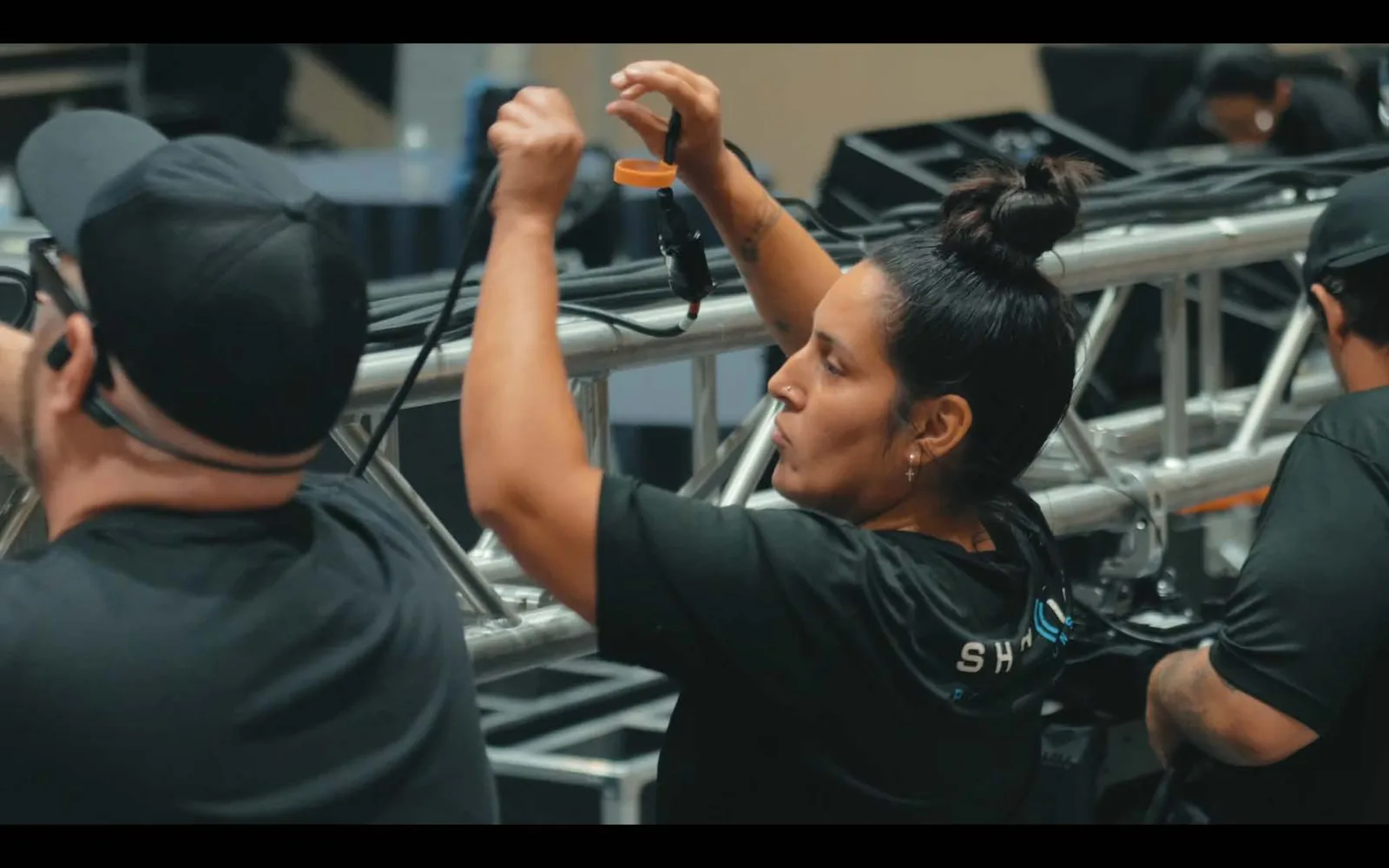 Crew member rigging a microphone capsule on truss backstage