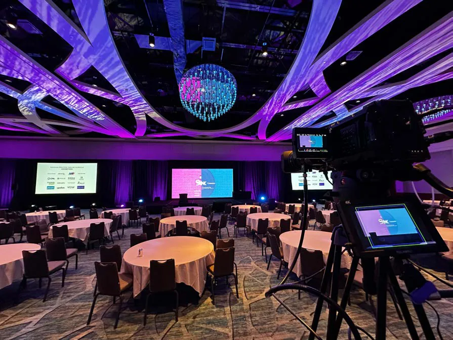 Conference general session room with banquet rounds and a broadcast camera