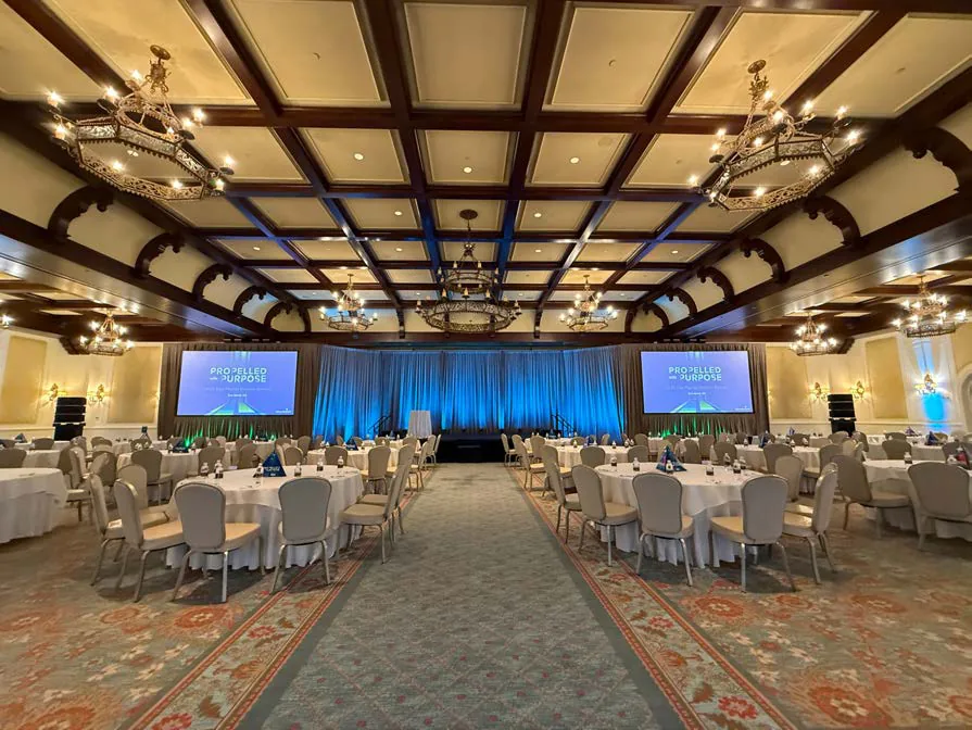 Healthcare general session with center aisle, drape, stage screens, and chandeliers