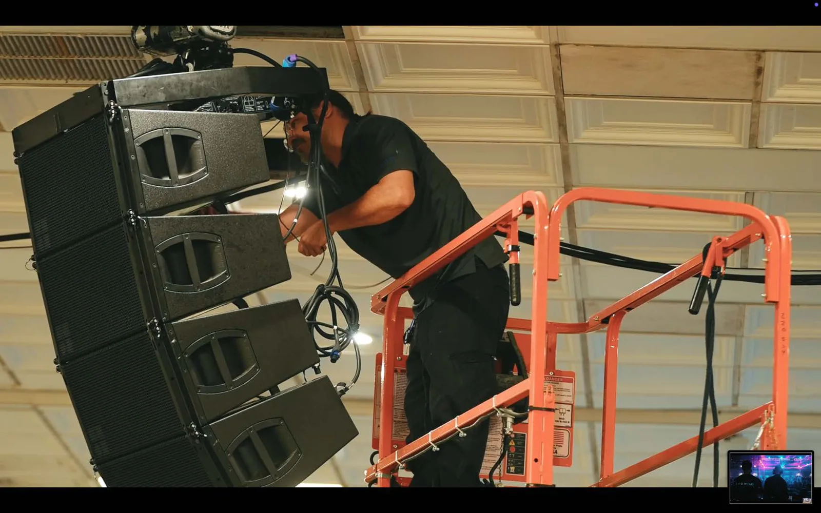 Technician rigging a hanging line array speaker cluster from a boom lift