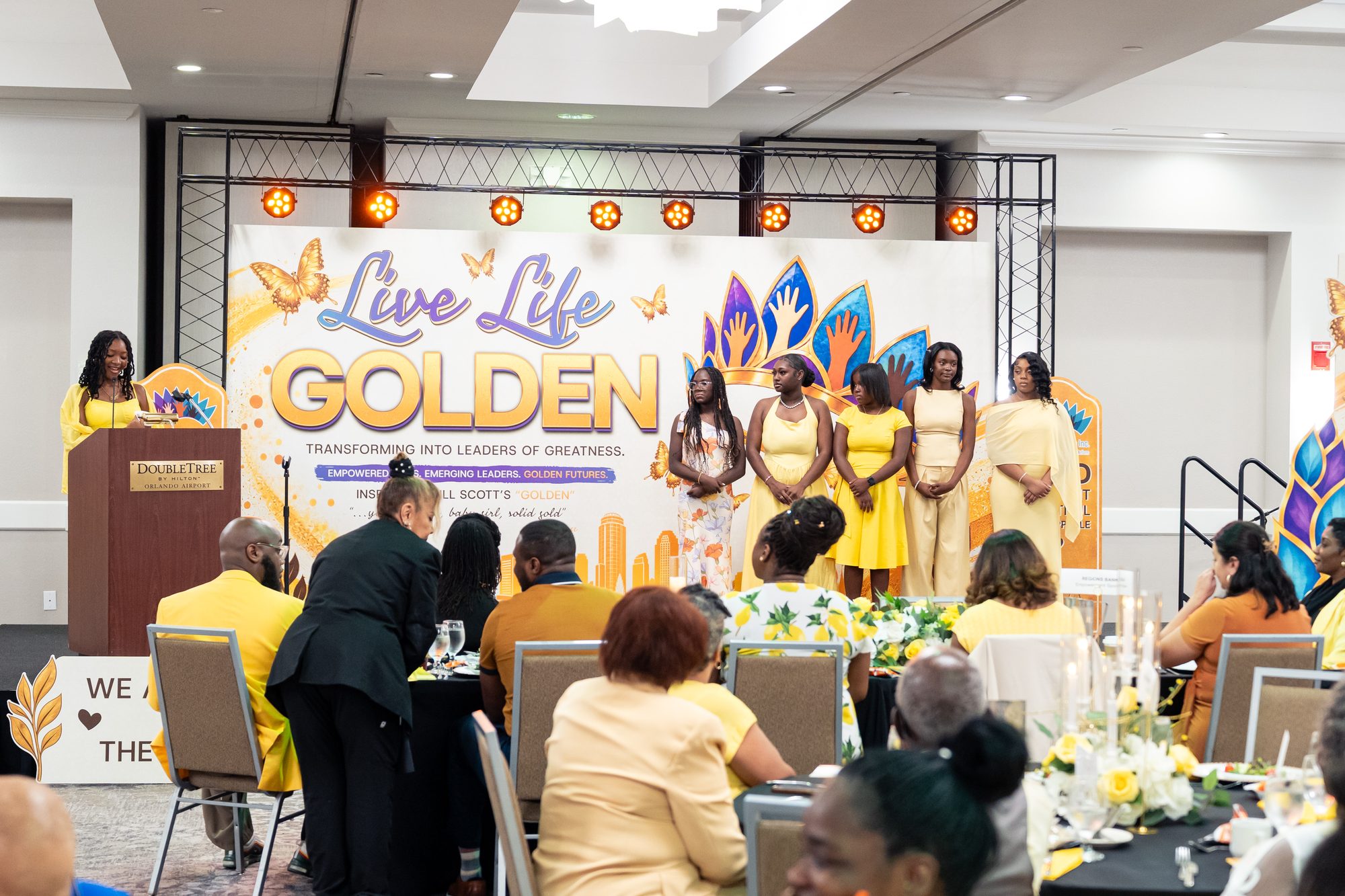 Girls on stage during the opening program, with guests at their tables