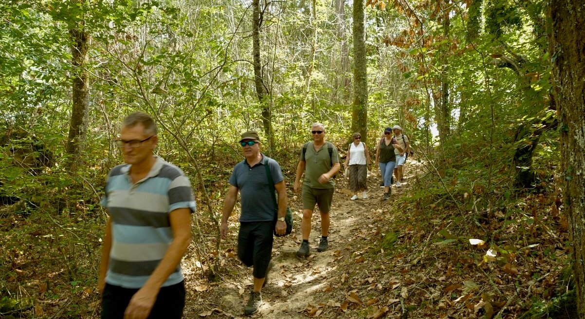 A group of people walking on a dirt trail through the woods.