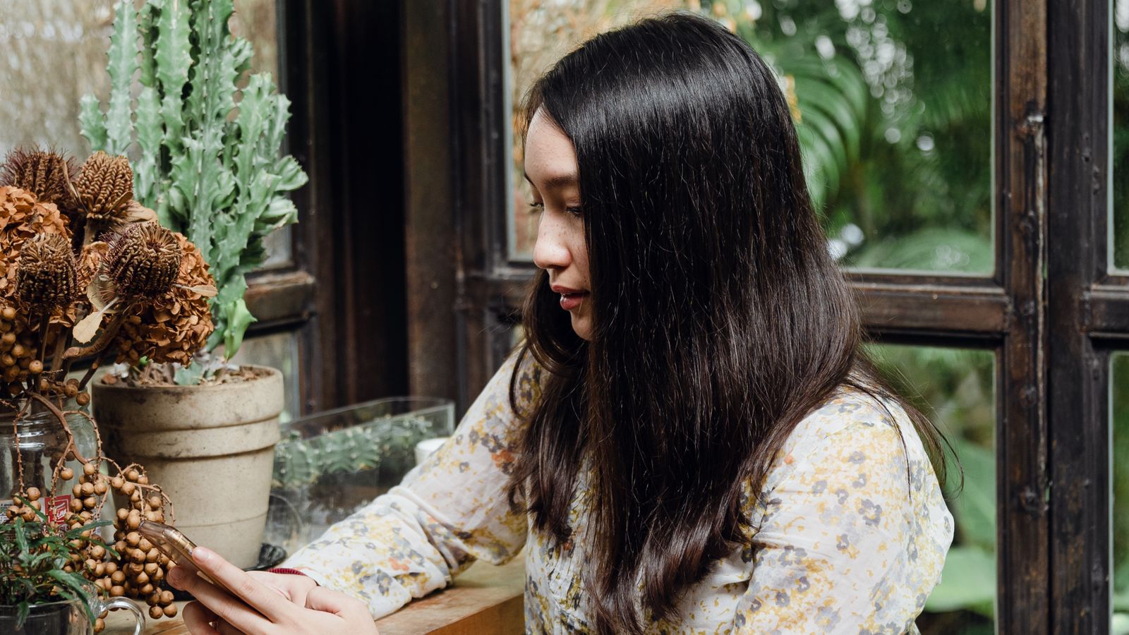 Focused young Asian lady texting on smartphone against window